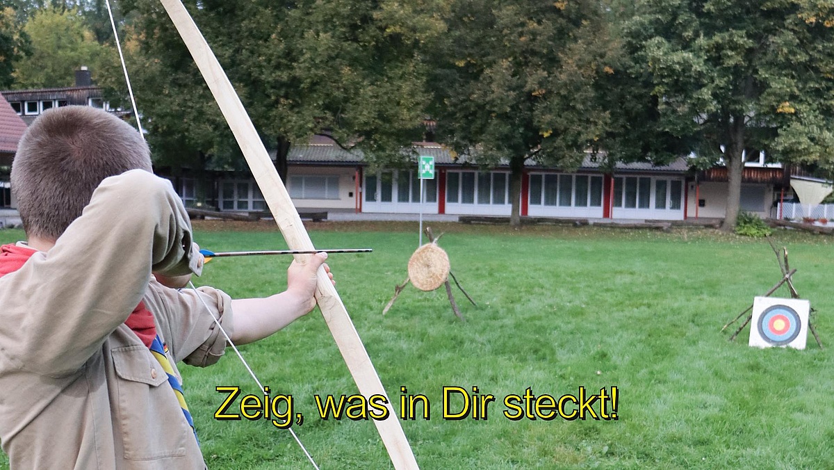 Ein Pfadfinder schießt mit Pfeil und Bogen.