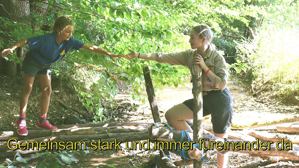 Eine Pfadfinderin aus Sindelfingen hilft einer anderen beim Überqueren eines Steges.